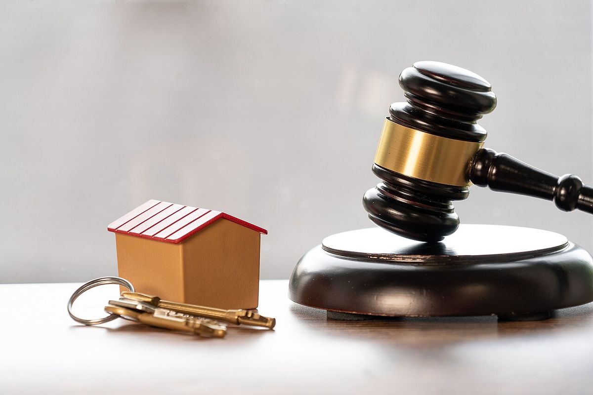 In this photo depicting property law and the process of buying a house, a gavel and block can be seen alongside a set of keys and house. We 