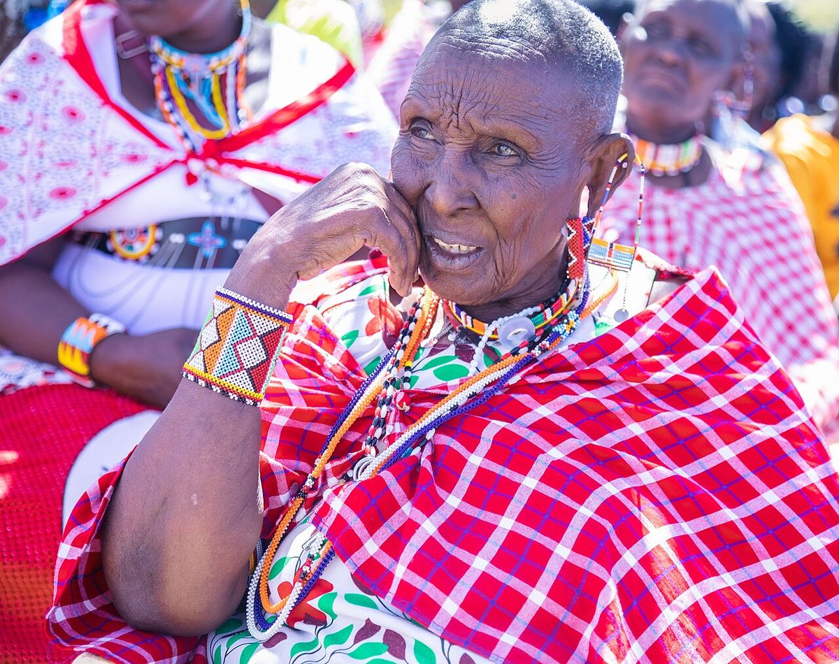 An elderly Maasai woman sits attentively during a community session in Kajiado County, Kenya. Adorned in traditional beadwork and a red shúk