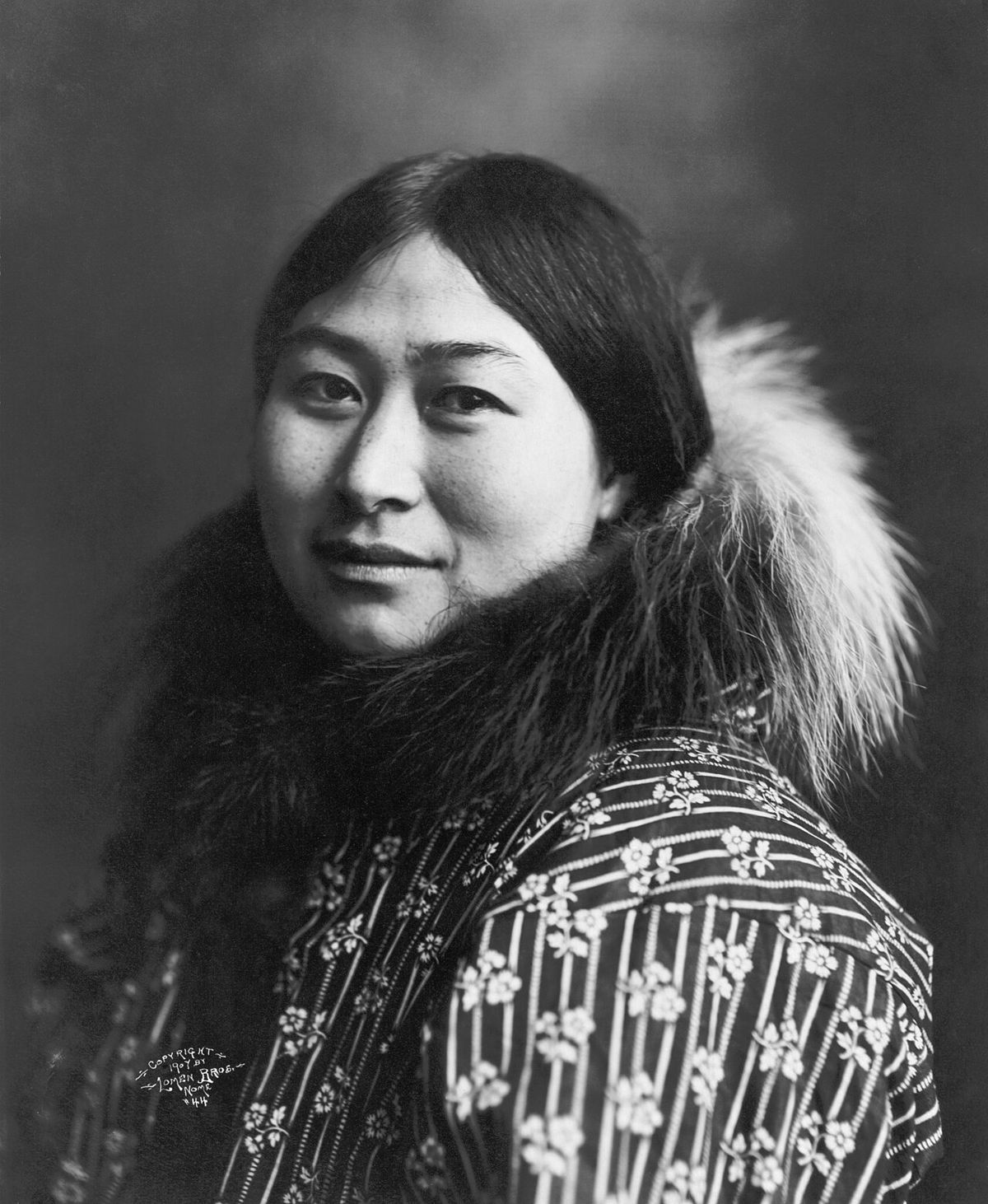 Photograph of Nowadluk/Nowadlook (Nora) Ootenna wearing a parka with a fur-lined hood. Ootenna was an Inupiat woman who was a popular subjec