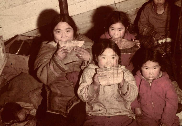 Title / Titre : Inuit women and children soften sealskin by chewing it, Nunavut / Des femmes et des enfants inuits mâchent des peaux de phoq