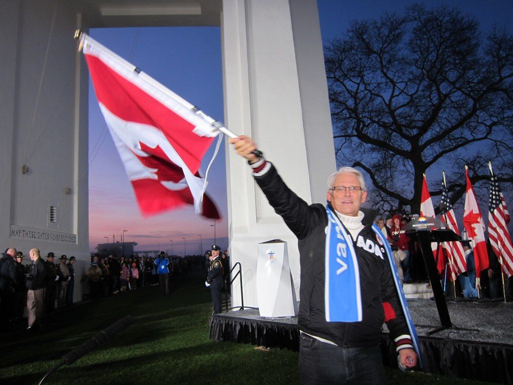 British Columbia Gordon Campbell waves the Canadian flag at the foot of the Peace Arch on the Canada - U.S. Border as the Olympic Flame make