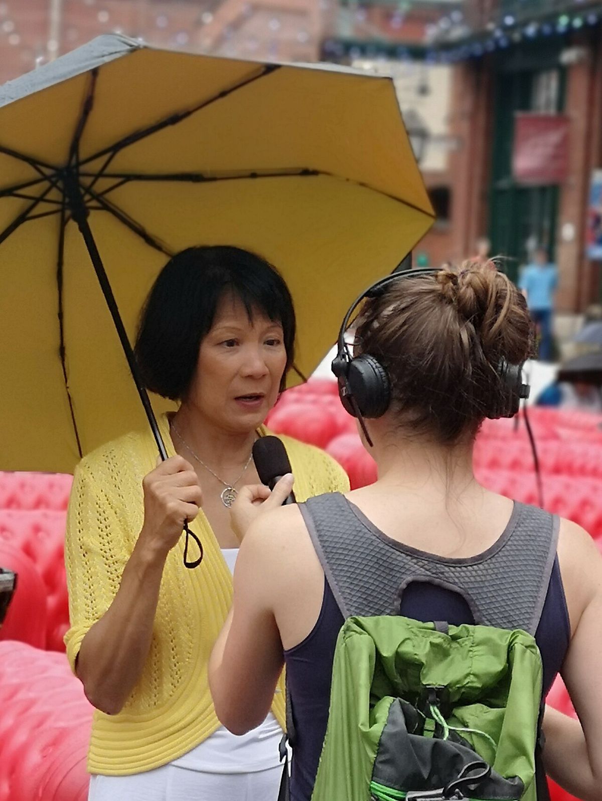 Une femme sous un parasol s'entretient avec une journaliste, de dos.